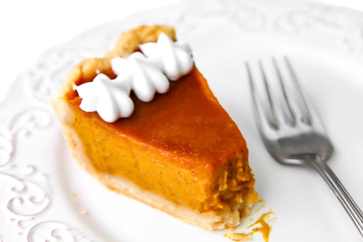 A slice of a vegan pumpkin pie on a white plate with a fork next to it.