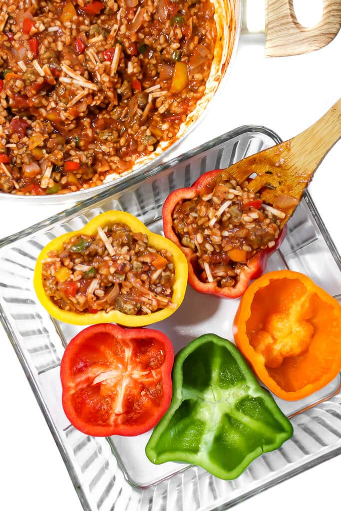 Colorful peppers in a baking dish being filled with a vegan pepper stuffing.