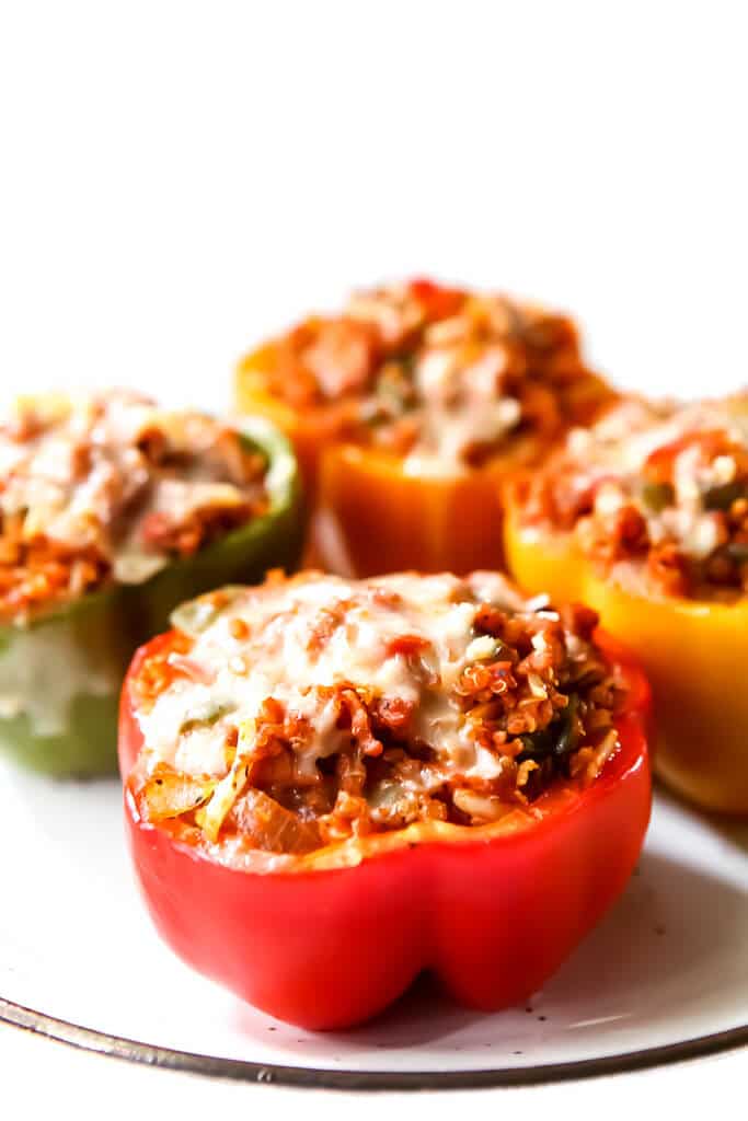 Four multi-colored vegan stuffed peppers topped with vegan cheese.