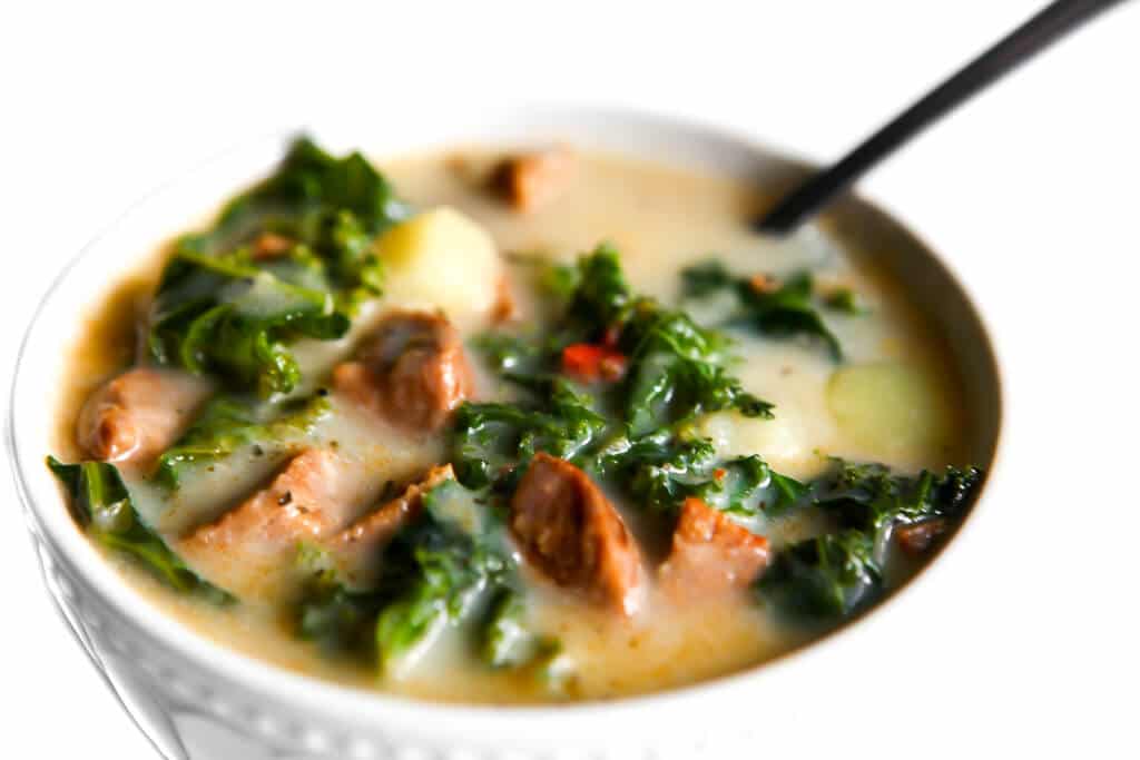 Plant-based zuppa toscana in a white bowl with a spoon sticking out of it.