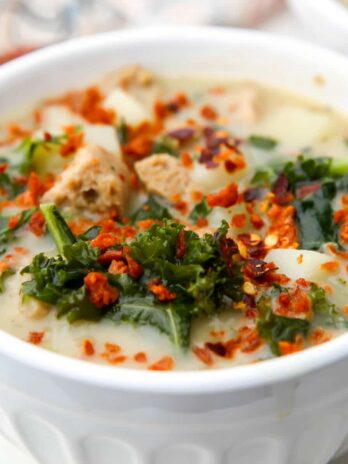 A white bowl filled with Zuppa Toscana with a tea towel behind it.
