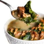 A spoonful of vegan zuppa toscana in a white bowl.