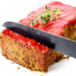 A vegan lentil loaf with ketchup on the top being cut with a knife.