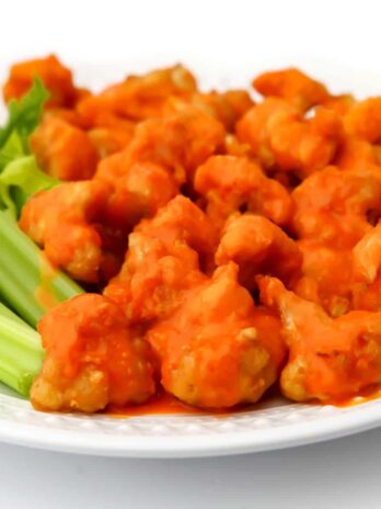 A white plate filled with vegan buffalo cauliflower nuggets with celery on the side.