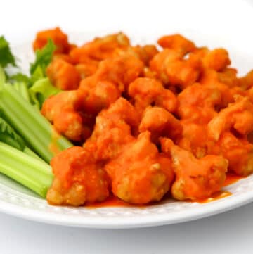 A white plate filled with vegan buffalo cauliflower nuggets with celery on the side.
