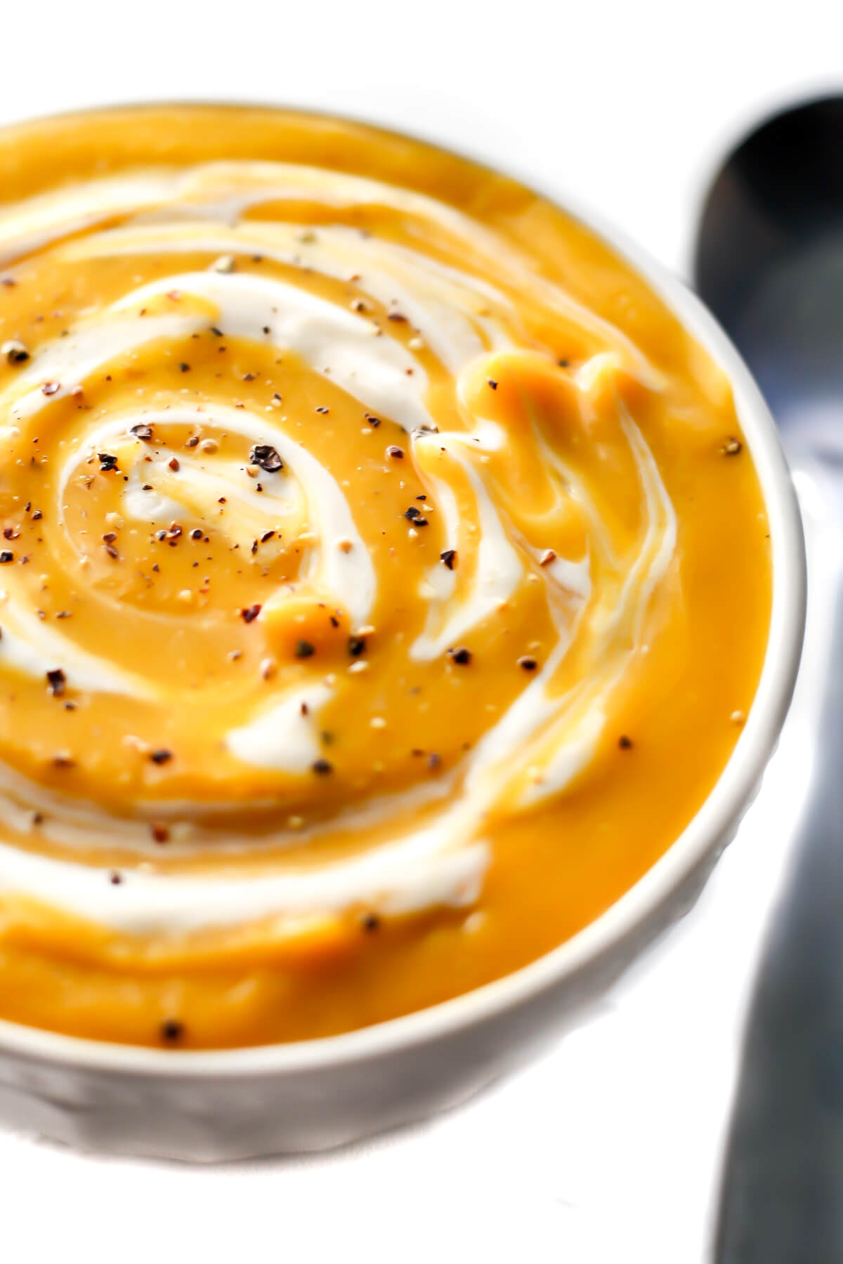 A bowl of vegan butternut squash soup with vegan sour cream swirled into it.