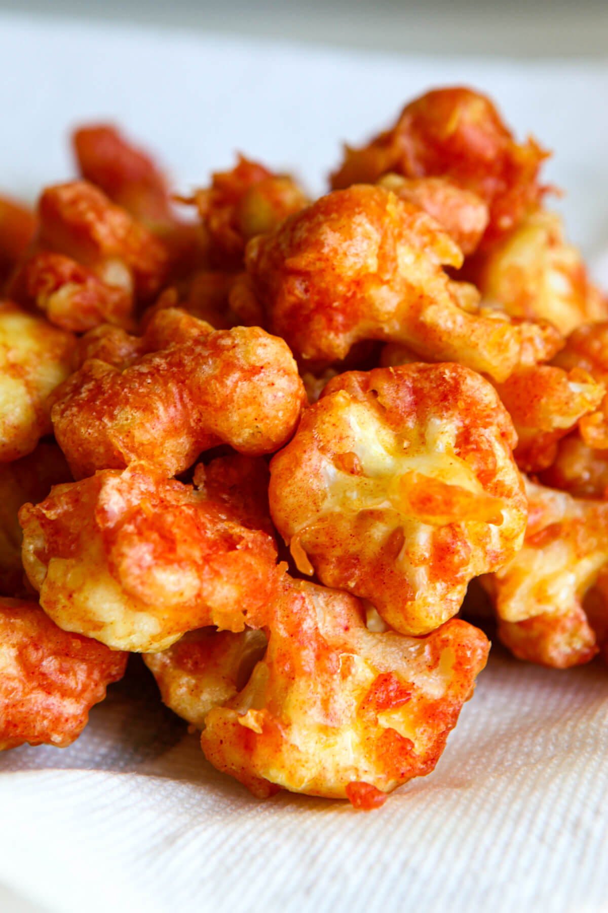 Lightly breaded and deep-fried cauliflower nuggets, that are then placed on a paper towel after frying.