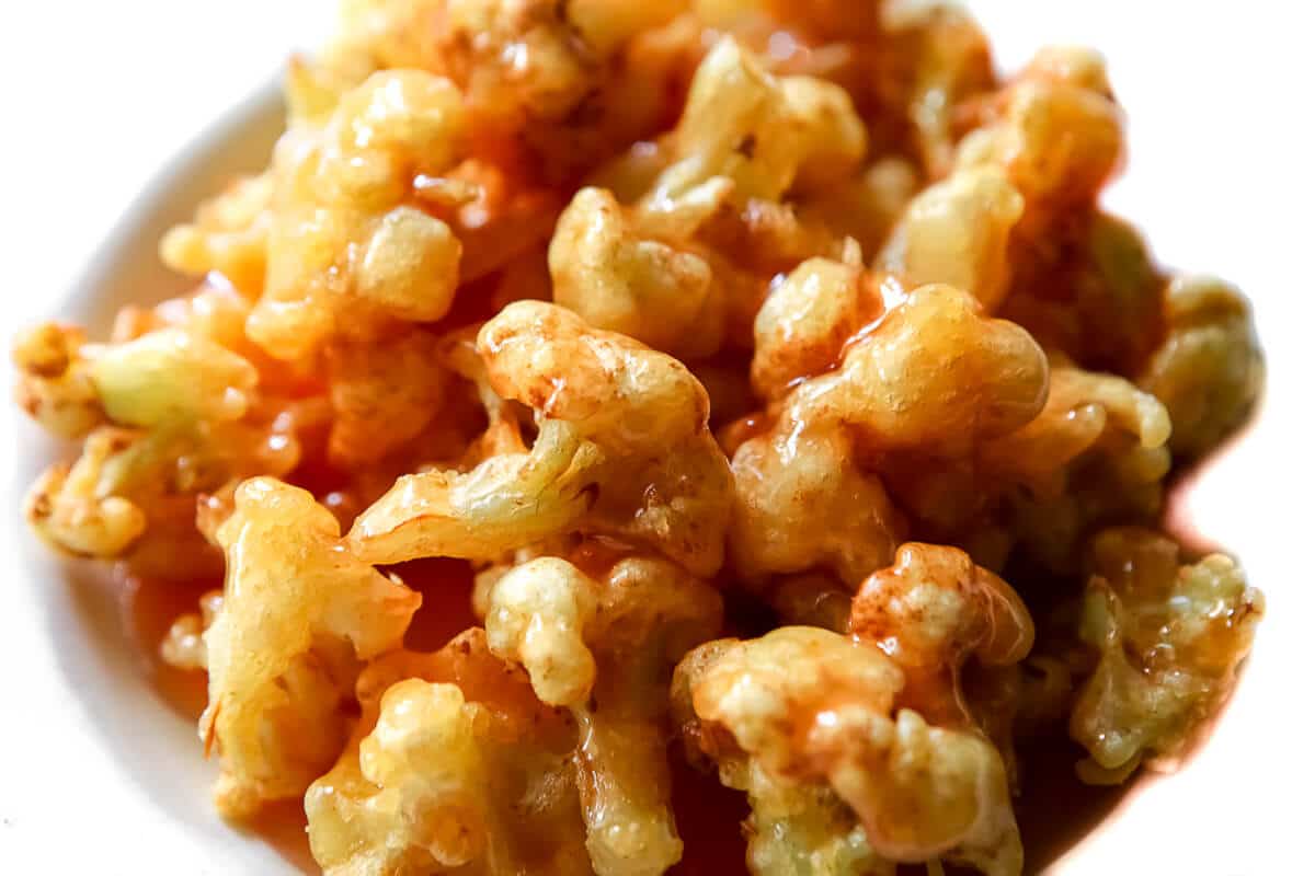 A top view of a bowl of deep-fried cauliflower with orange sauce drizzled over it.