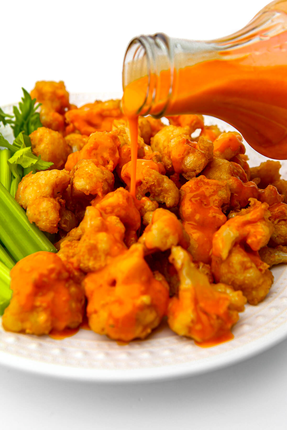 Vegan buffalo sauce being poured over fried cauliflower.