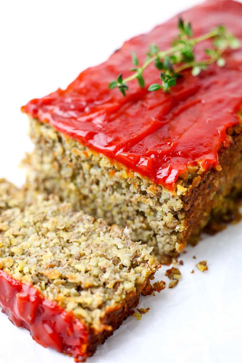 A lentil loaf topped with ketchup with a slice cut.
