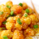 A close up of sticky orange cauliflower with sesame seeds and green onions on top.