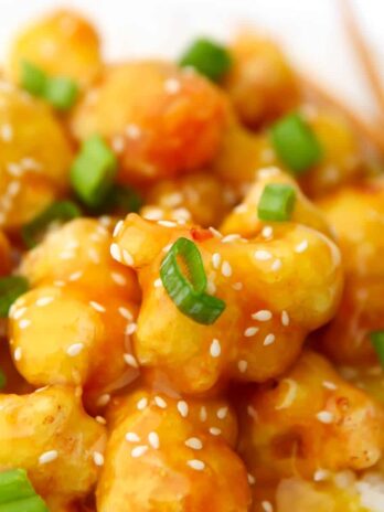 A close up of sticky orange cauliflower with sesame seeds and green onions on top.