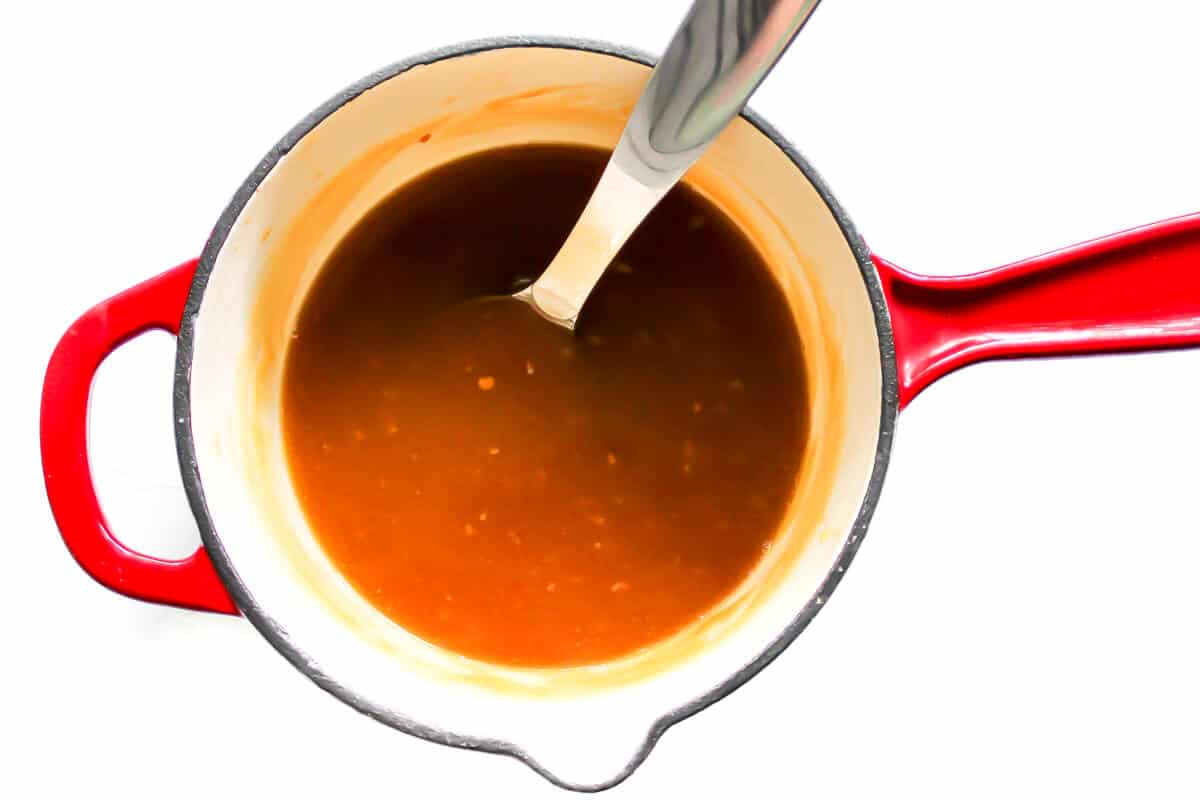A red sauce pan filled will homemade orange sauce for making orange "chicken," cauliflower, and tofu.