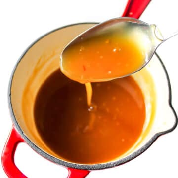 A red saucepan filled with Chinese style orange sauce.