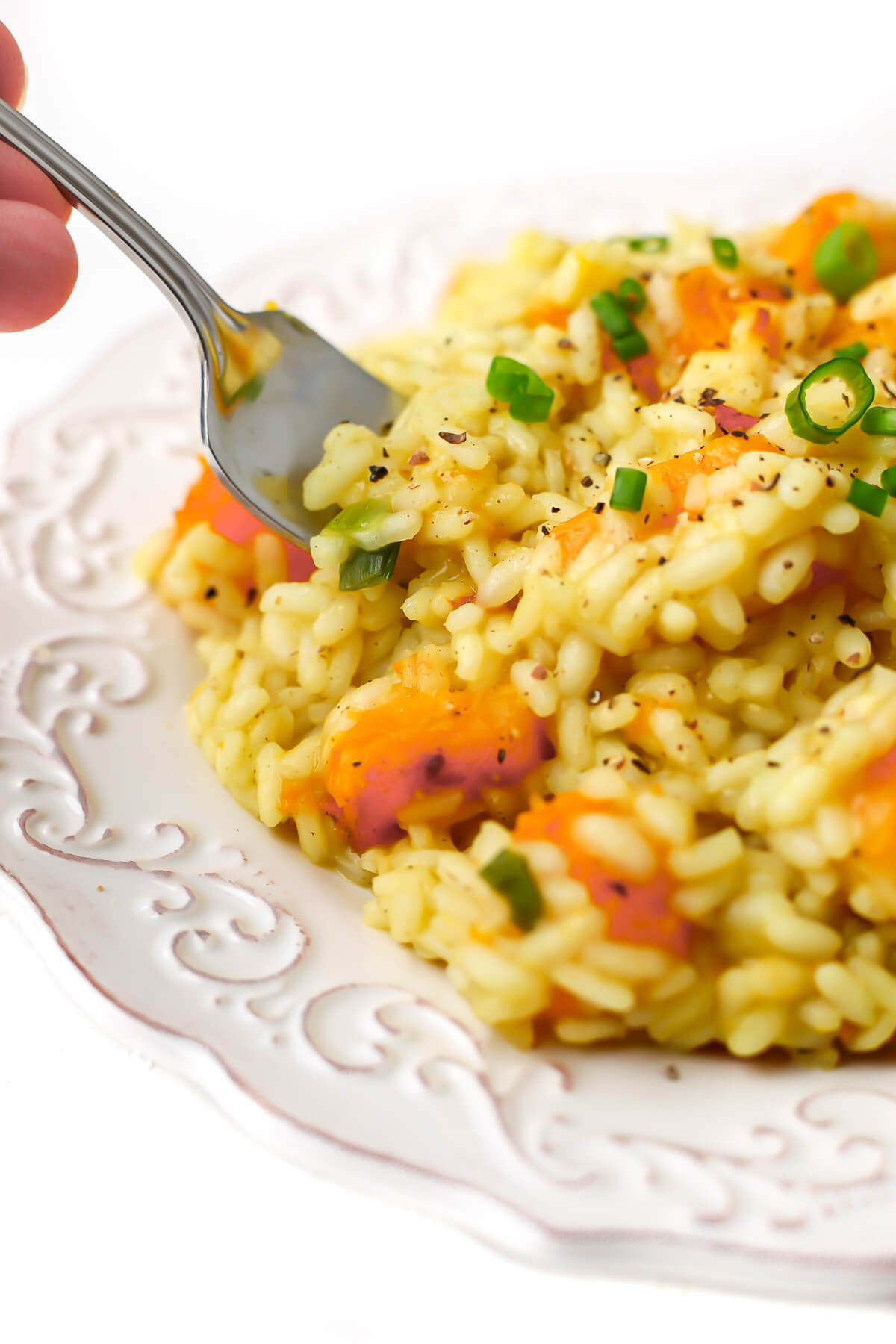 A plate of vegan butternut squash risotto with someone taking a fork full.