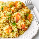 A close up of vegan squash risotto on a white plate with a fork on the side.