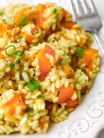 A close up of vegan squash risotto on a white plate with a fork on the side.