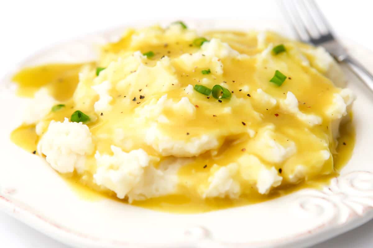 A white plate full of mashed potatoes and gravy with chives sprinkled on top.