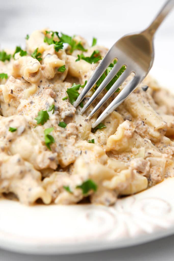 A close up of vegan stroganoff topped with parsley with a fork sticking in it.