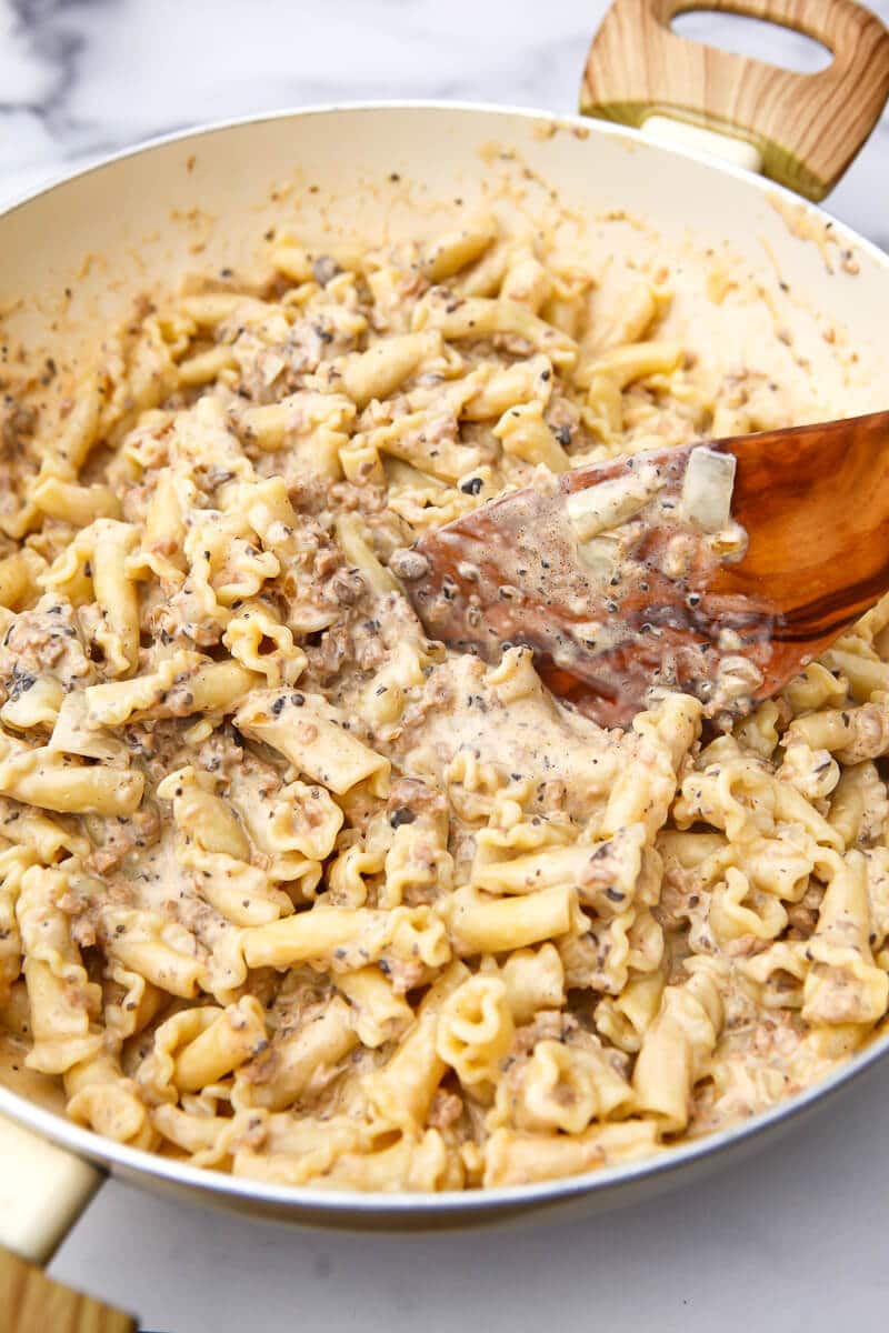 A large wok filled with a creamy vegan stroganoff sauce mixing with noodles.