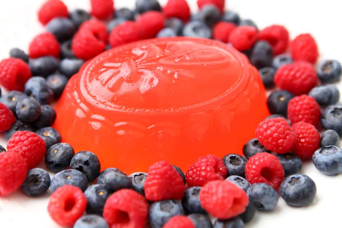 A vegan jello mold on a white plate with berries around it.