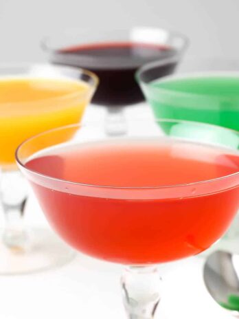 Four glasses full of vegan jello in orange, strawberry, grape and lime flavors.