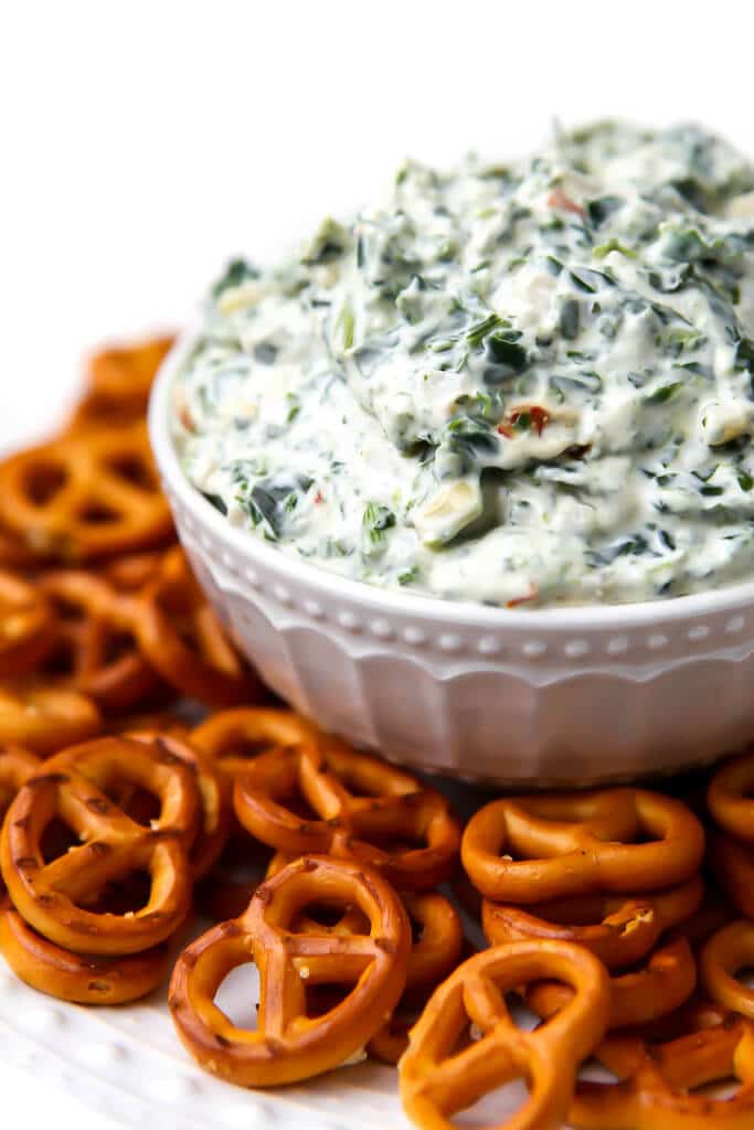 A bowl of creamy vegan spinach dip with pretzels around it. . 