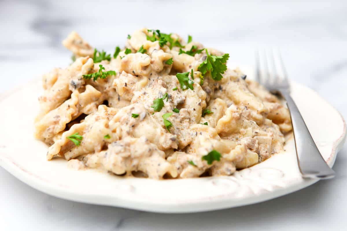 A creamy vegan "beef" stroganoff on a white plate with a fork on the side.