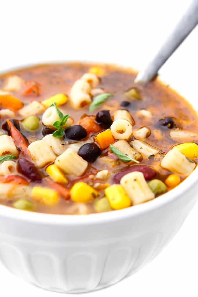 A white bowl filled with vegetarian minestrone soup with a spoon in it. 