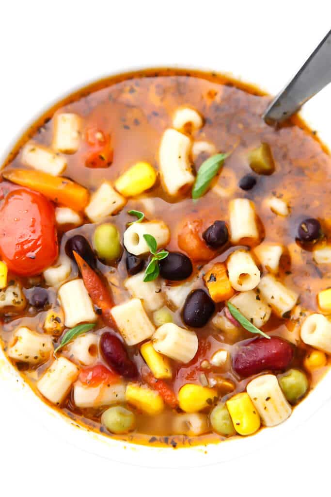A top view of a bowl of vegetarian minestrone soup with tomatoes, pasta, veggies, and beans. 