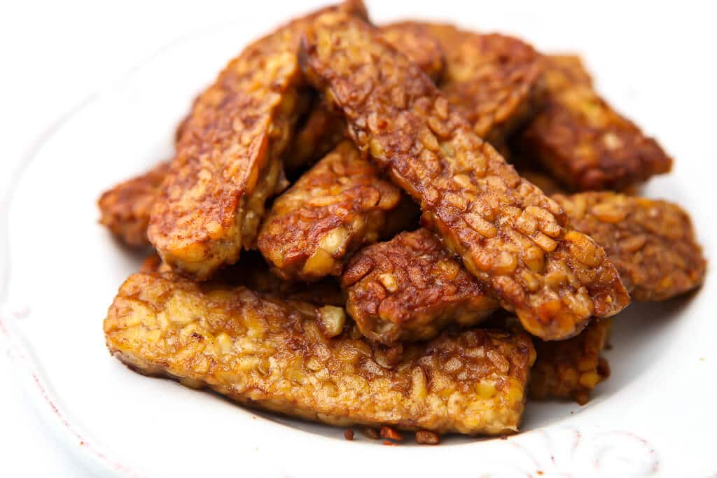 A pile of vegan tempeh bacon on a white plate.
