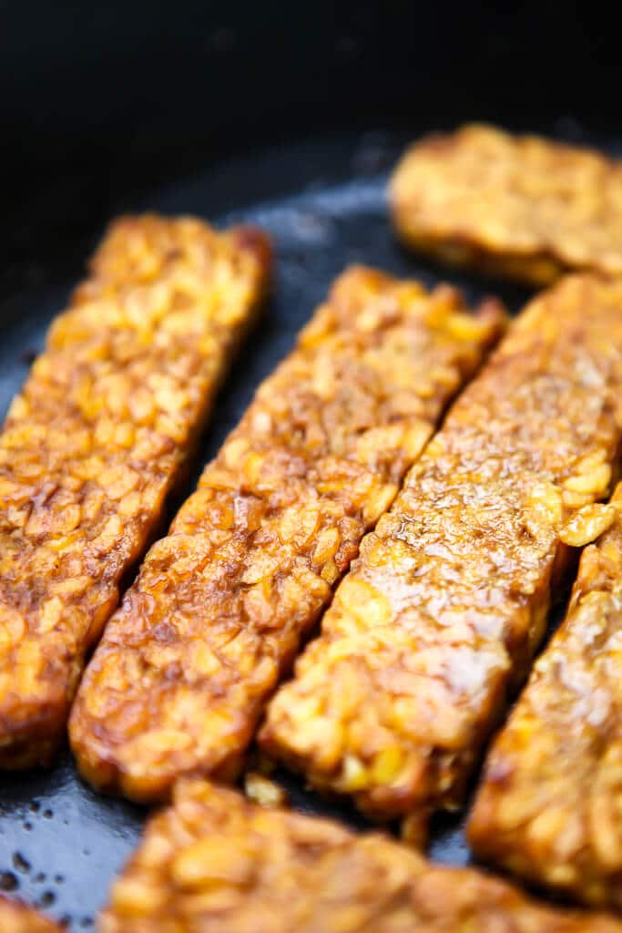 Vegan tempeh bacon frying in a pan.