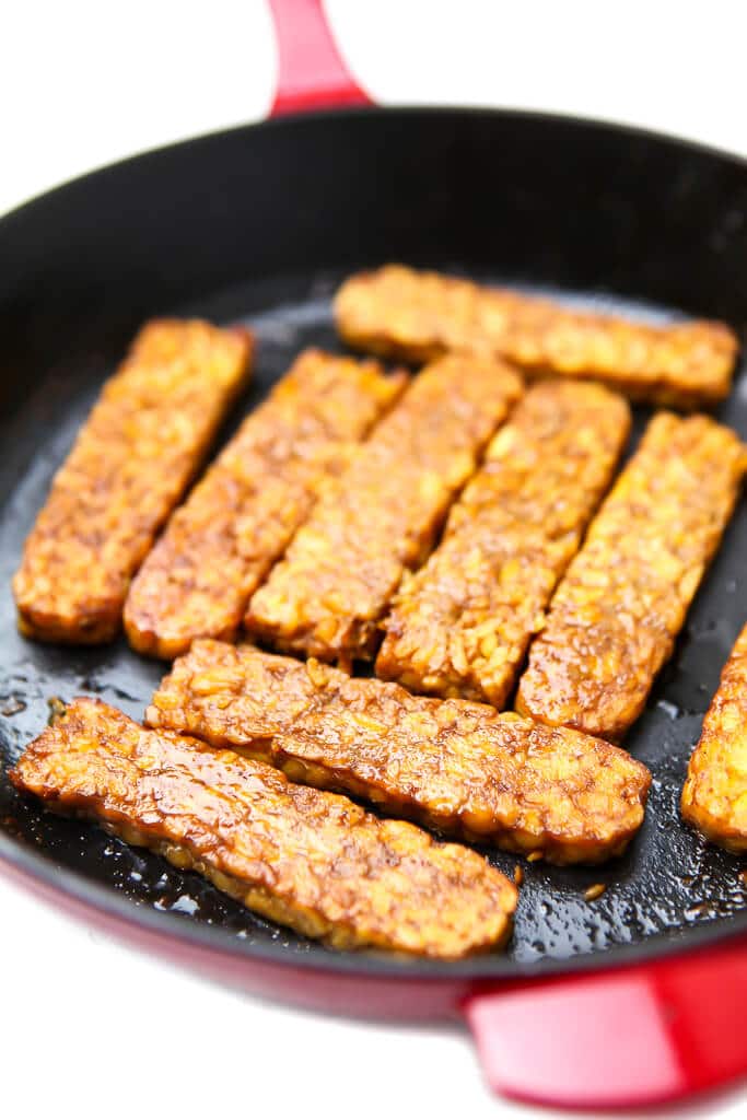 A red frying pan filled with bacon flavored tempeh cooking.
