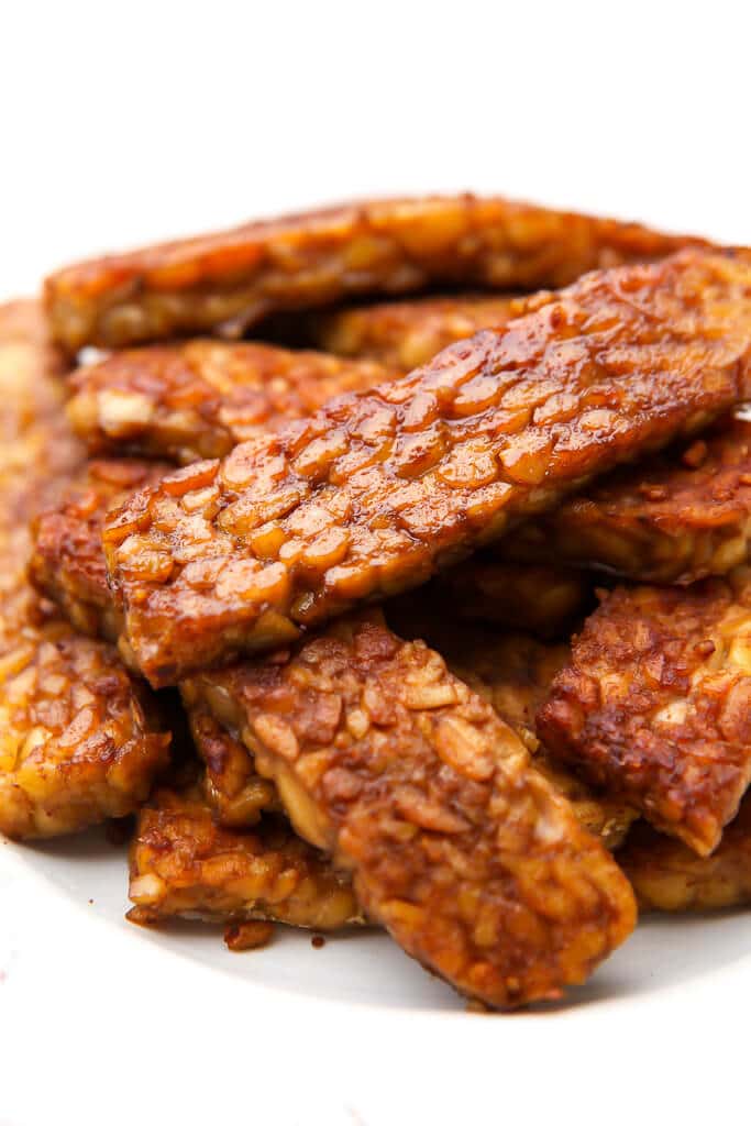 A pile of cooked vegan tempeh bacon on a white plate.