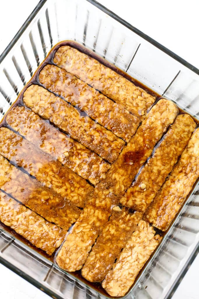 Strips of tempeh marinating in a smoky sauce to make tempeh bacon.