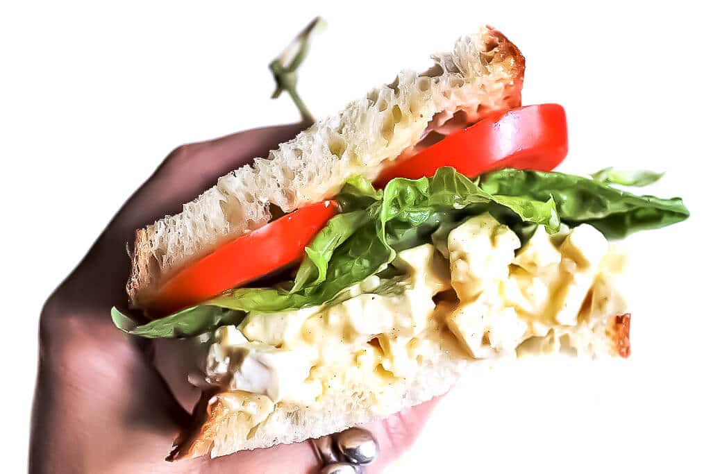 A vegan tofu egg salad sandwich in someone's hand ready to take a bite.