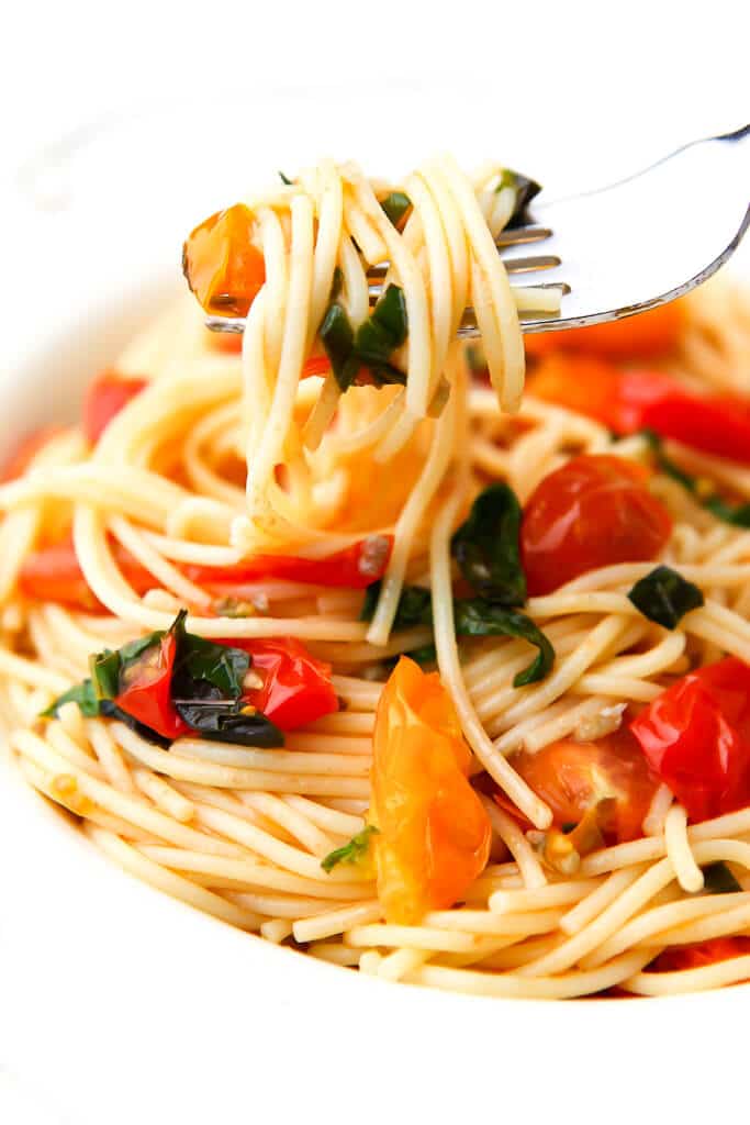 A fork full of tomato basil spaghetti on a white plate. 