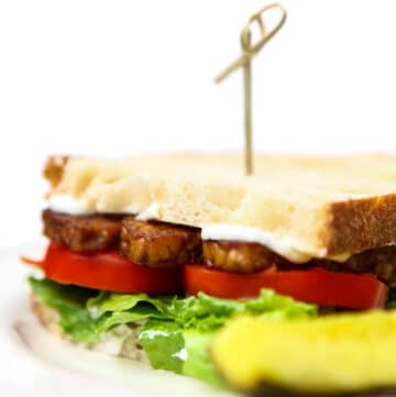 A close up of a vegan bacon, lettuce and tomato sandwich on a white plate.