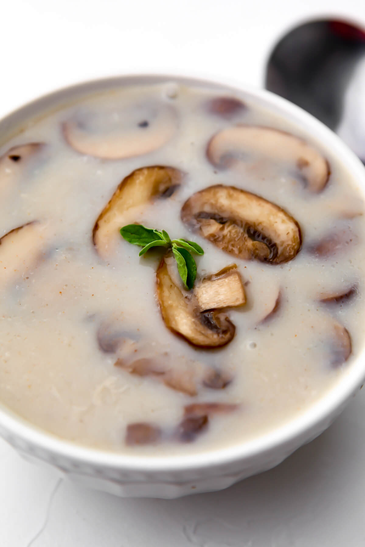 A white bowl filled with vegan cream of mushroom soup with a spoon on the side.