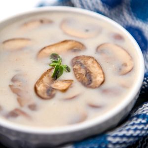 A bowl of vegan cream of mushroom soup with a blue tea towel on the side.