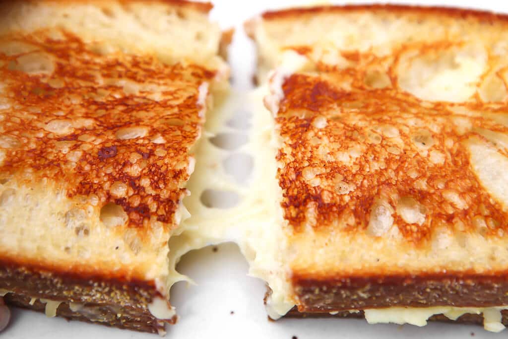 A vegan grilled cheese sandwich being pulled apart showing how it melts and stretches.