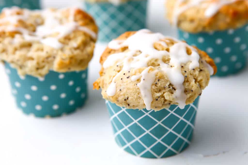 Three lemon poppy seed muffins in blue cupcake liners with lemon drizzle on top of them.