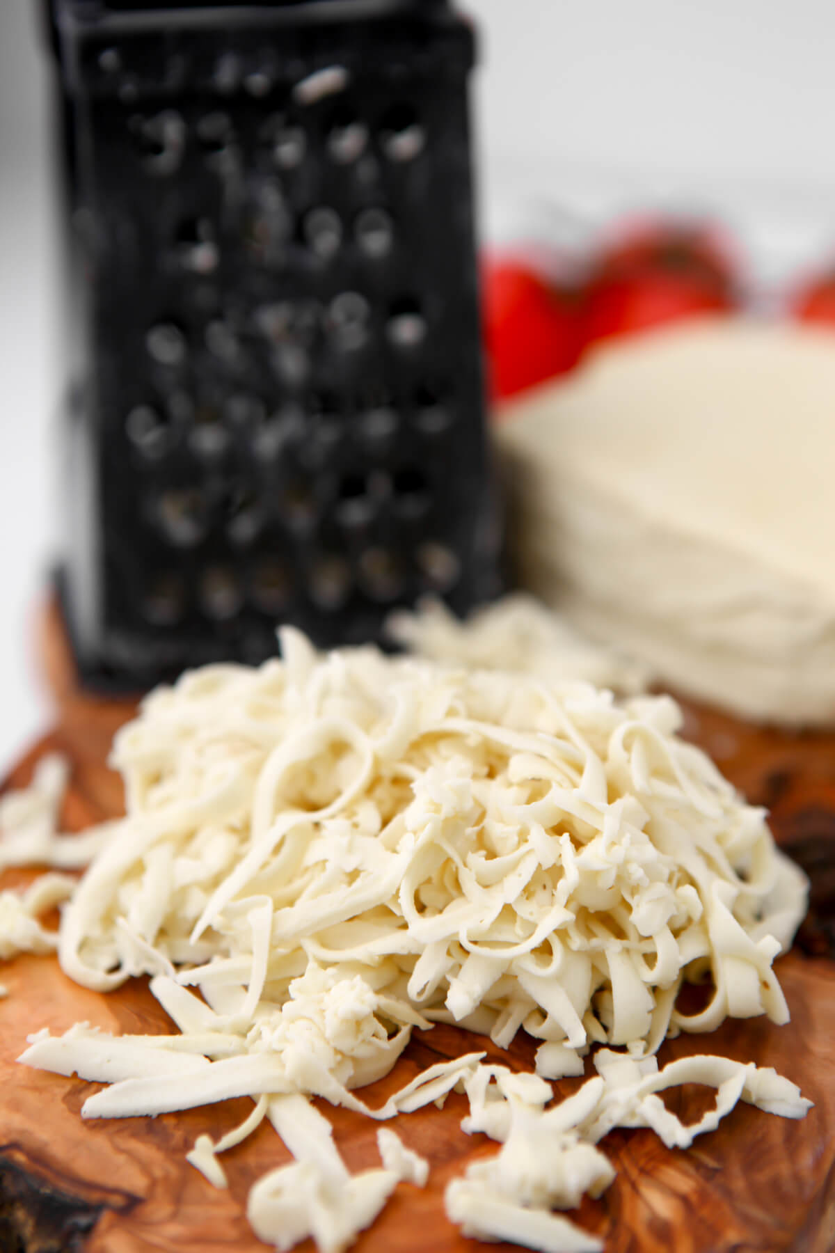Shredded vegan mozzarella cheese on a cutting board next to a cheese grater. 