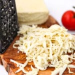 A block of vegan mozzarella cheese on a cutting board with a cheese grater and some of it shredded.
