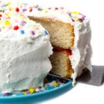 A slice being taken out of a vegan vanilla cake with vanilla buttercream frosting.