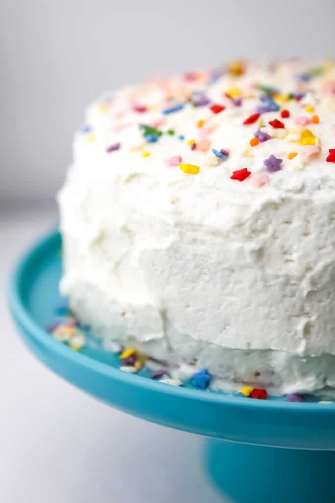 A white cake with colorful sprinkles on a blue cake dish.