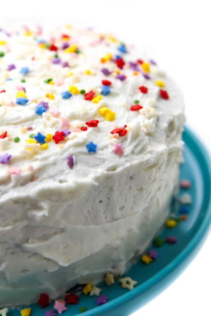 A vegan vanilla cake with vanilla buttercream on a blue cake dish topped with sprinkles.