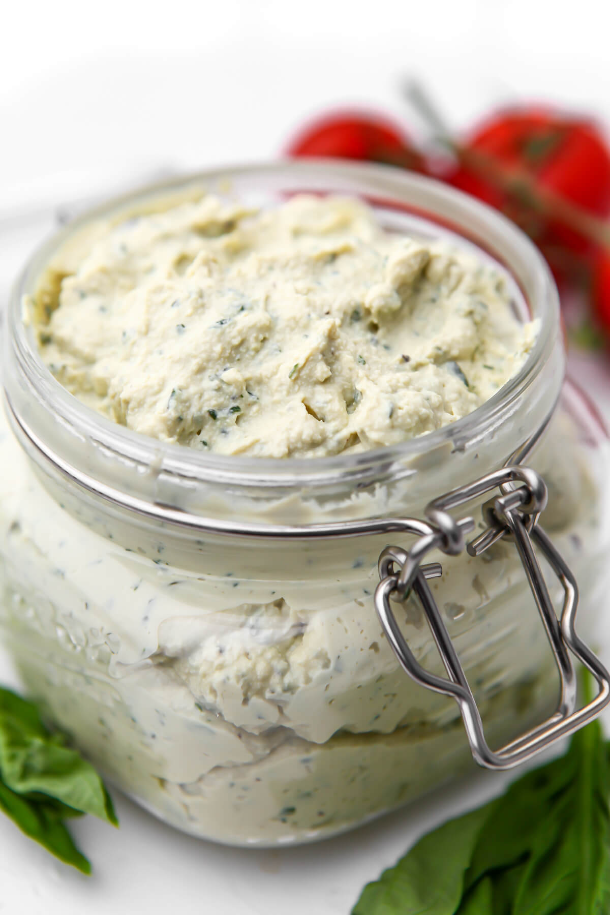 A glass jar filled with vegan ricotta made from tofu with tomatoes behind it.
