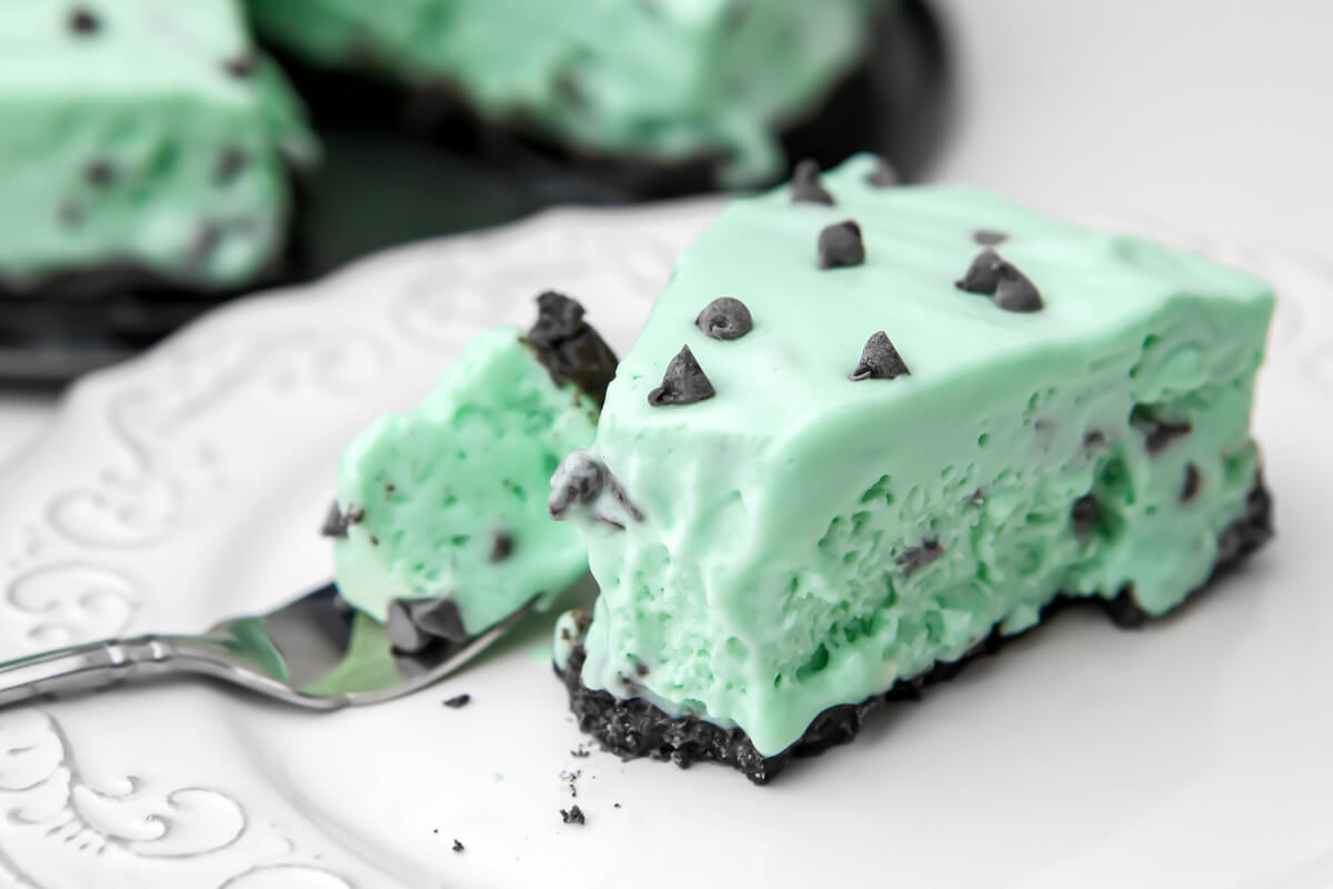 A slice of frozen vegan grasshopper pie on a white plate with more pie behind it.