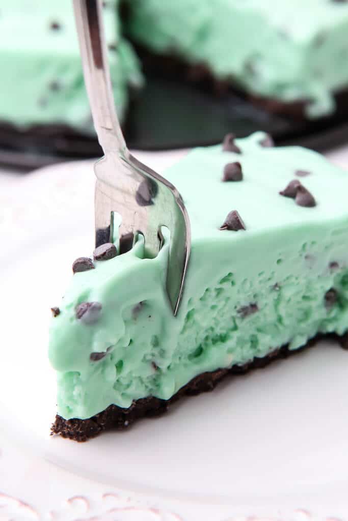 A slice of vegan mint green grasshopper pie with a fork in it on a white plate